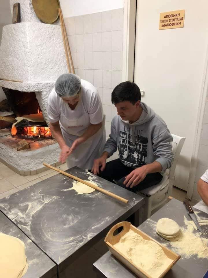 woman teaching a boy how to use wood dough paddles to make pies at 'Agios Antonios Women’s Agri Cooperative'